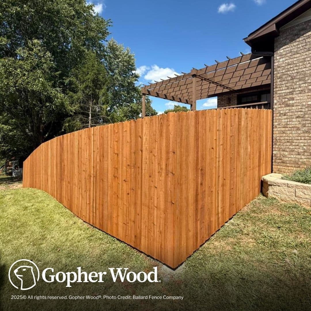 Tall wooden privacy fence with dog-ear pickets on a lawn beside a brick house.
