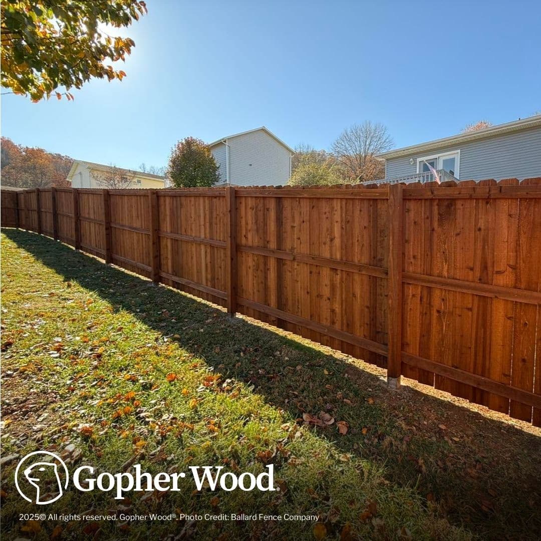 Tall brown wooden privacy fence bordering a grassy backyard under a clear blue sky.
