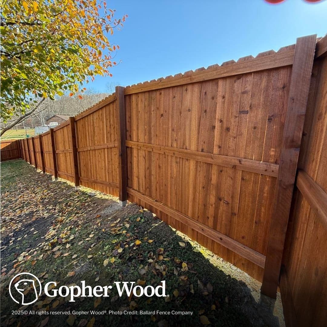 Stained brown wooden privacy fence panels installed on a slope with scattered autumn leaves.