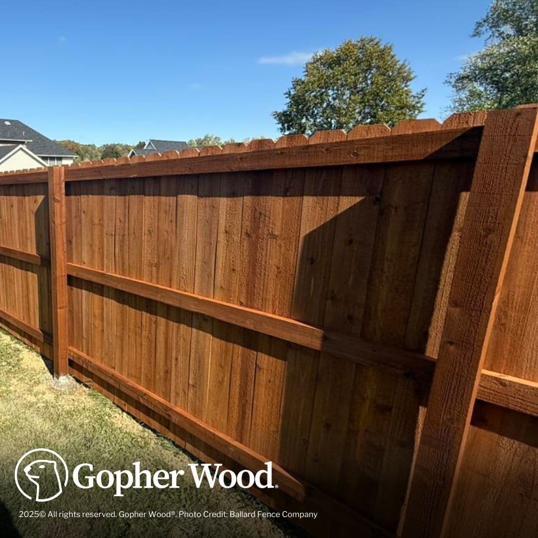 Stained brown wooden privacy fence with dog-ear pickets and horizontal rails in the sunlight.