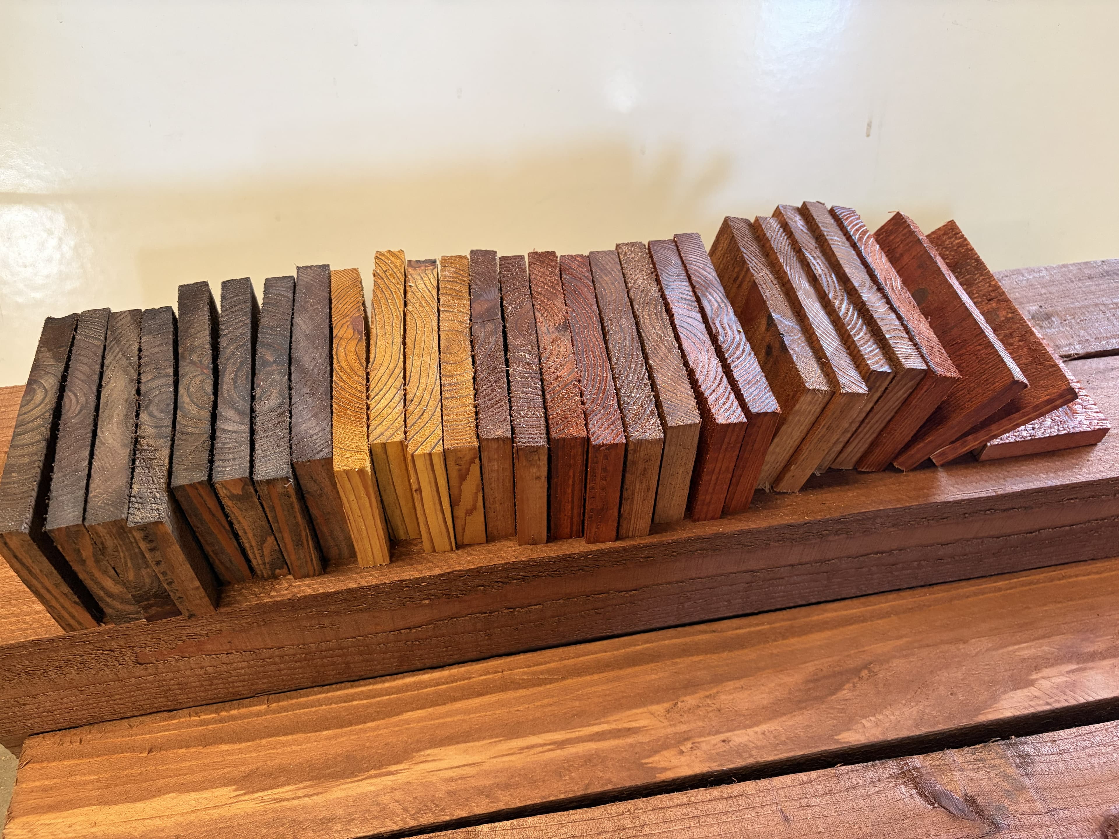 A row of small wood blocks displaying a variety of stain colors and grain patterns.